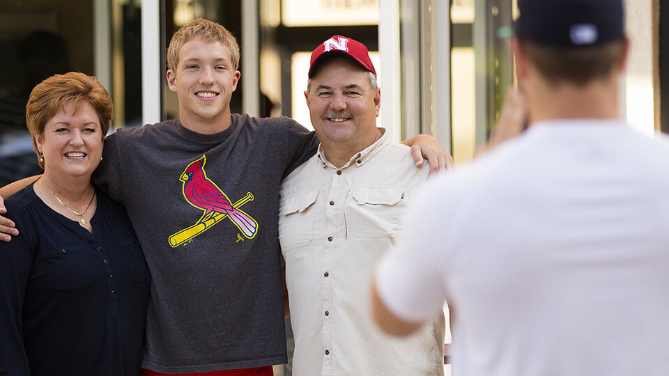 Young man with parents flanking them on either side held in a hug.